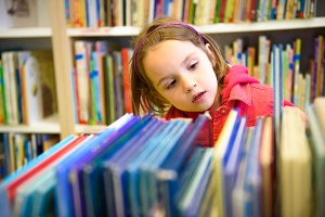 zaciekawiona dziewczynka wybiera ksiazki w bibliotece