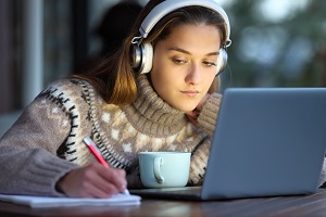 uczennica w swetrze robi notatki przy wlaczonym laptopie