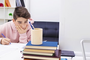 chlopiec odrabia lekcje przy biurku z ksiazkami