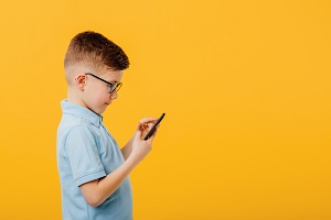 chlopiec skupiony na smartfonie na zoltym tle