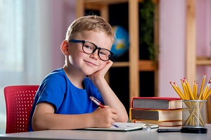 usmiechniety chlopiec siedzi przy biurku i odrabia lekcje
