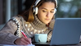 uczennica w swetrze robi notatki przy wlaczonym laptopie